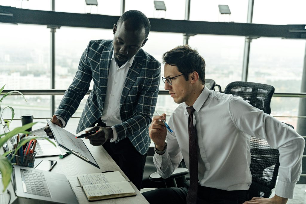 Two businessmen collaborate in a modern office setting, engaged in a focused discussion.